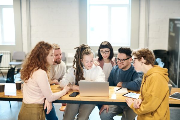 Valokuva, jossa kuusi henkilöä kerääntyneenä tietokoneen ääreen kehittämään iloisina yrityksen strategiatyötä.